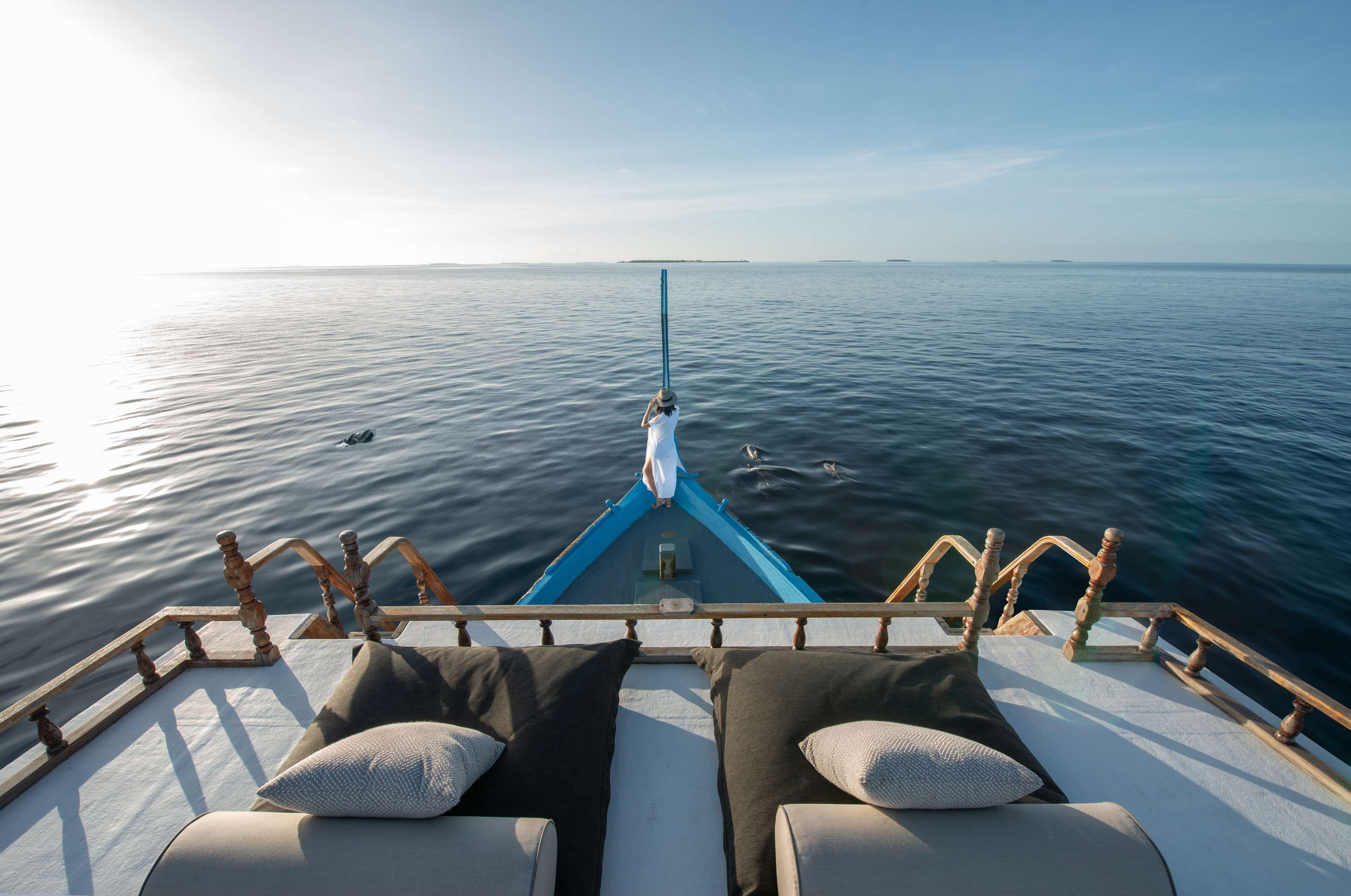 A boat deck with two cushioned seating areas facing the water, a railing, and a clear view of the sea.