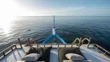 A boat deck with two cushioned seating areas facing the water, a railing, and a clear view of the sea.