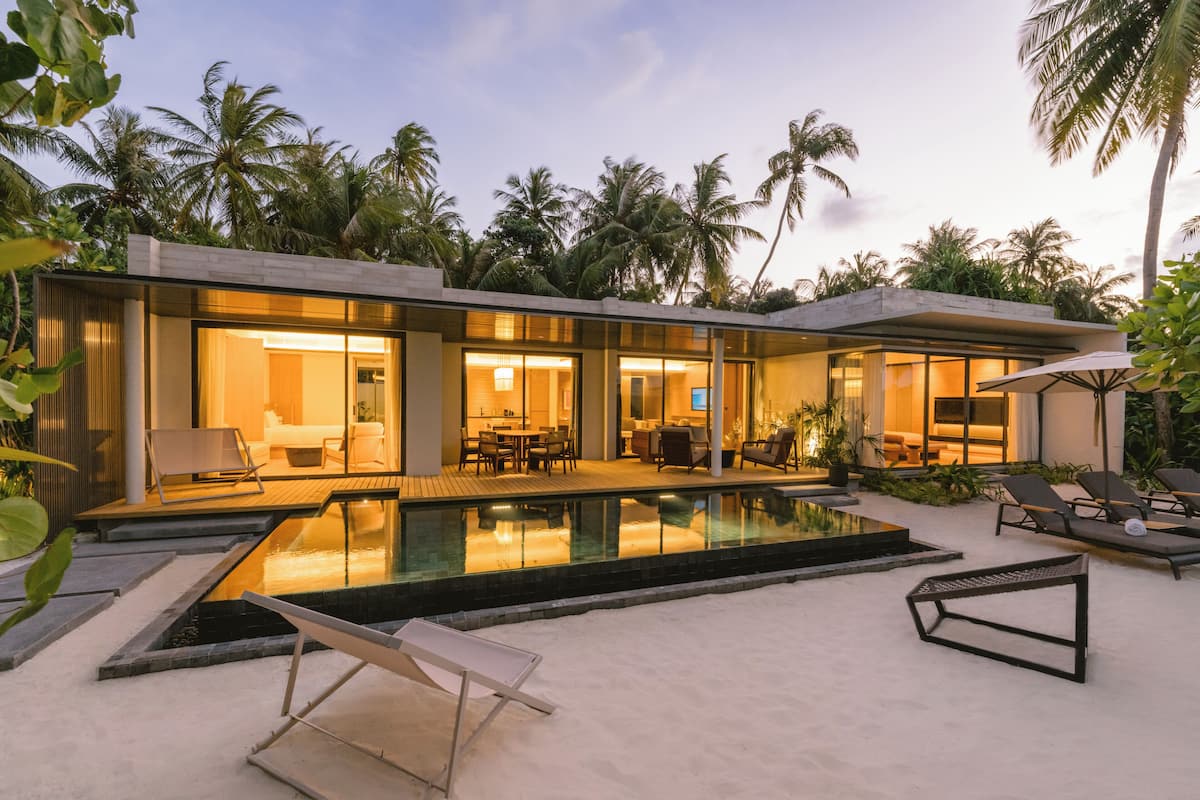 Una casa moderna con piscina, mobiliario exterior y palmeras.