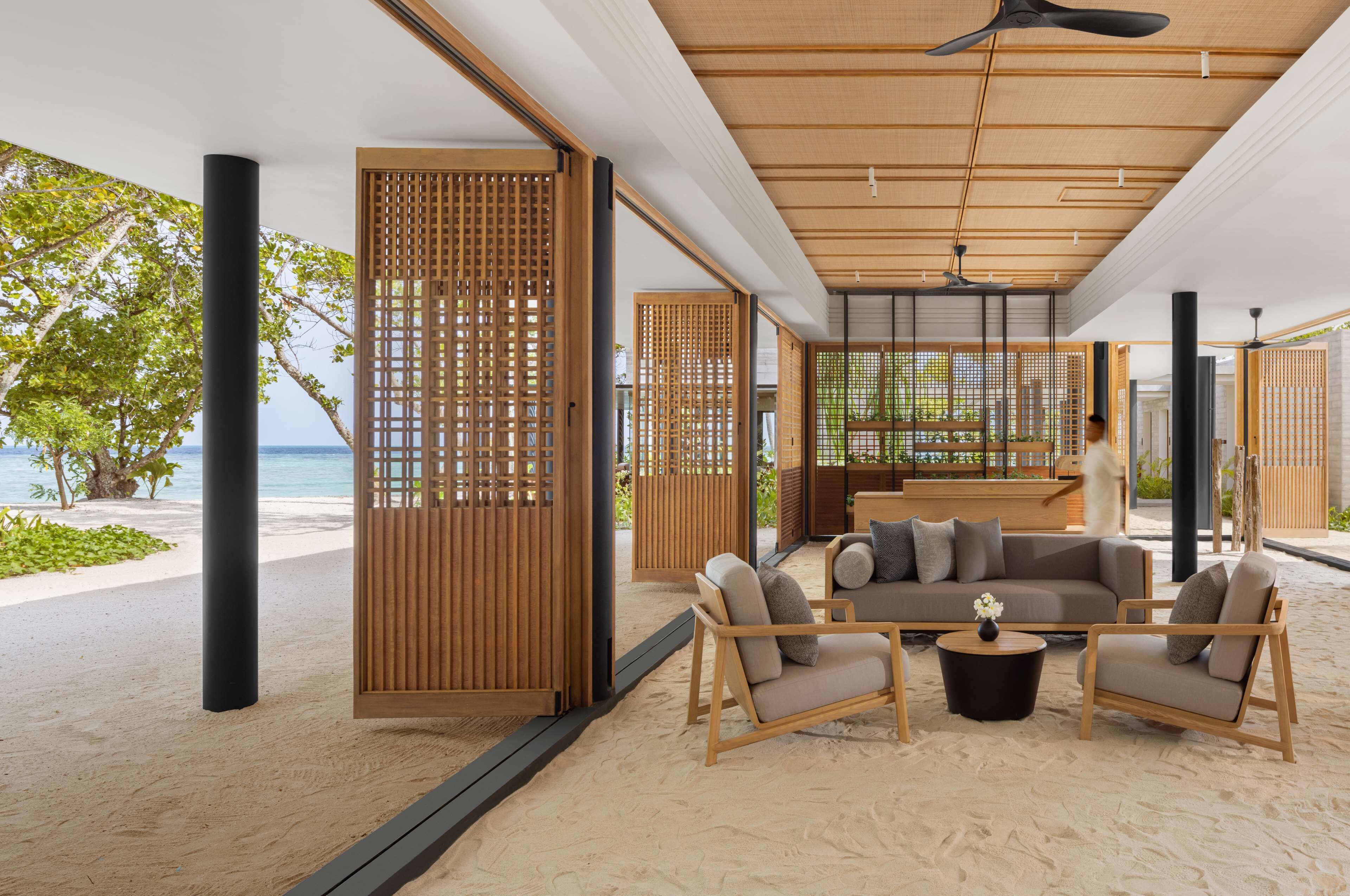 Une chambre située en bord de mer, avec un plafond en bois, un canapé, deux fauteuils et une table basse.
