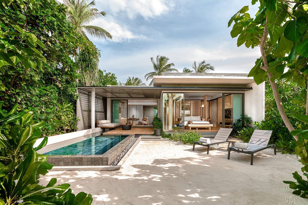 Una casa moderna con piscina, mobiliario exterior y abundante vegetación.