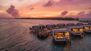 Bungalows sobre el agua con terrazas abiertas y vista al atardecer.