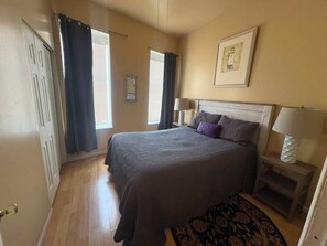 A bedroom with a bed, two bedside lamps, a headboard, a window with curtains, a door, and a framed picture on the wall. - Second Floor Apartment 1 block from Lafayette Park (St. Louis)