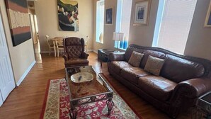 Ein Wohnzimmer mit braunem Ledersofa, einem gemusterten Teppich, Deckenventilator und gerahmten Kunstwerken an den Wänden.
