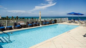 A pool area with lounge chairs and umbrellas, overlooking a clear blue ocean. - Boutique Suite with Ocean View and Rooftop Pool (Miami Beach)