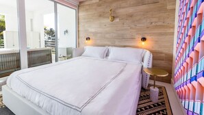 A modern bedroom with a large bed, a wooden accent wall, and a balcony with a view. - Boutique Suite with Ocean View and Rooftop Pool (Miami Beach)