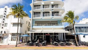A multi-story hotel with a curved facade, outdoor dining area, and palm trees. - Boutique Suite with Ocean View and Rooftop Pool (Miami Beach)