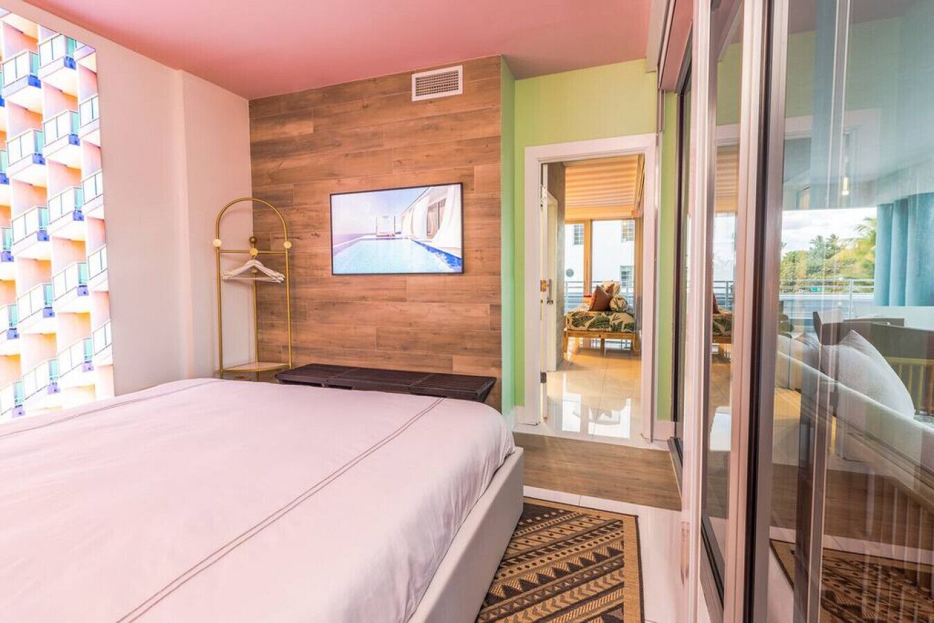 A hotel room with a bed, a TV mounted on the wall, a wooden accent wall, and a view of the outside balcony.