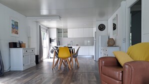 Et moderne køkken med hvide skabe, et spiseområde med en gul stol og en brun lædersofa.