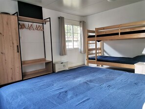 Ein Zimmer mit Etagenbett, Kleiderschrank, Schreibtisch und einem Fenster mit Vorhängen.