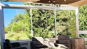 En udendørs siddeplads med fletmøbler, et pergola og udsigt til grønne områder.