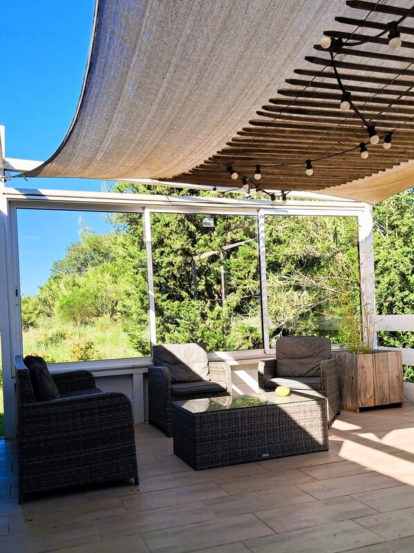 An outdoor seating area with wicker furniture, a pergola, and a view of greenery.