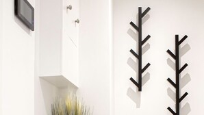 A modern hallway with a white wall, a black metal console table with a vase of plants, and two black wall-mounted decorations. - Stunning Flat / Walk to town & beach / Bournemouth (Bournemouth)