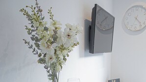 A dining table set with plates, cutlery, and glasses, a vase with flowers, a clock, and a small decorative item on a white wall. - Stunning Flat / Walk to town & beach / Bournemouth (Bournemouth)