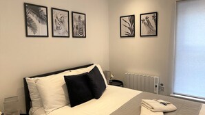 A hotel room with a bed, pillows, a nightstand, a radiator, and framed artwork on the wall. - Stunning Flat / Walk to town & beach / Bournemouth (Bournemouth)