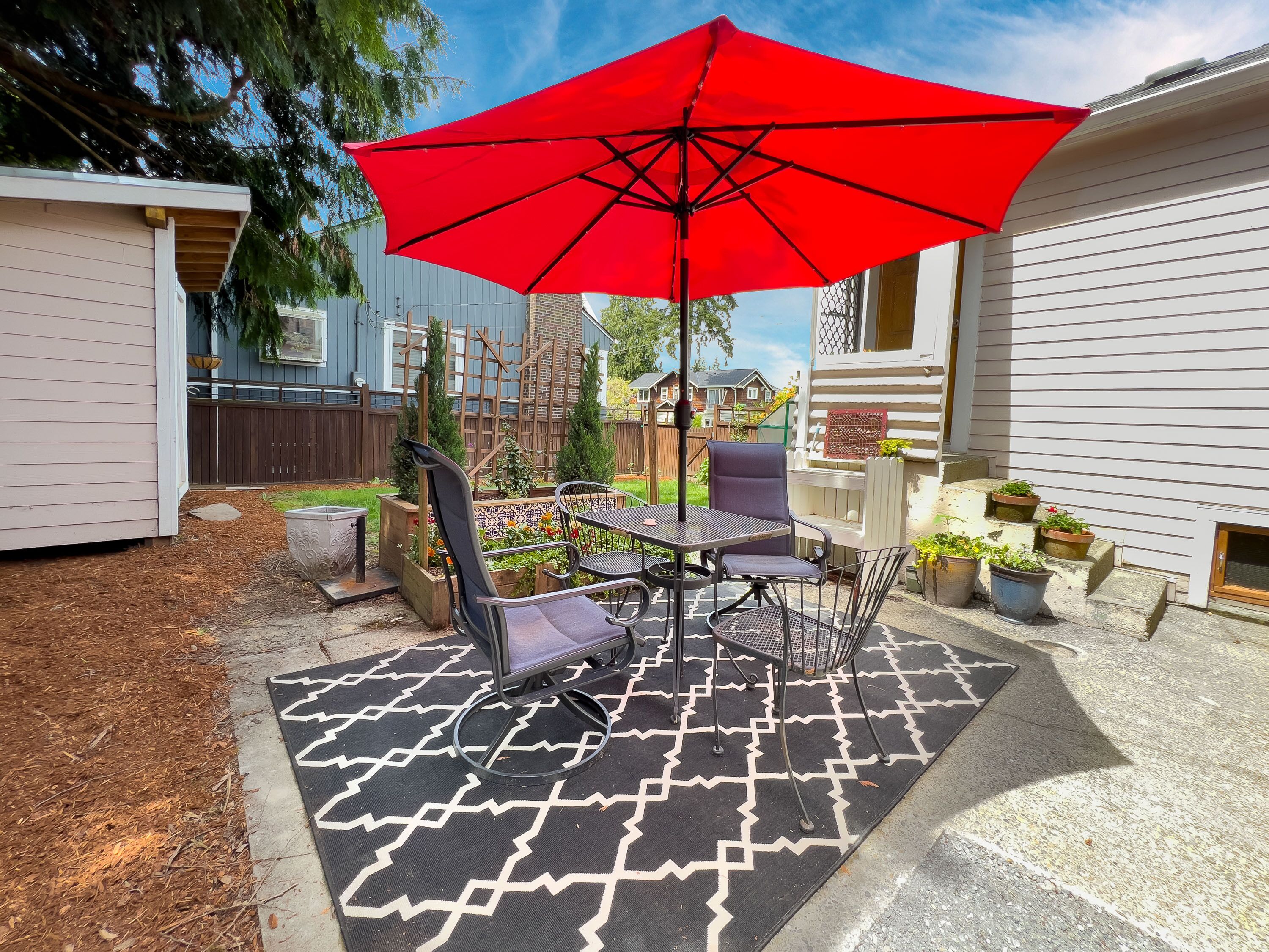 Une terrasse avec une table et des chaises, un parasol rouge et des plantes en pot.