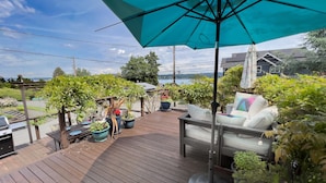 A wooden deck with outdoor furniture, a large umbrella, and potted plants. - 4bd w/ Lake Views and Chef's Kitchen (Seattle)