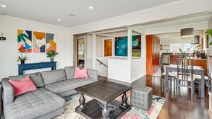 A modern living room with a grey sectional sofa, a dark wooden coffee table, and a dining area with a table and chairs. - 4bd w/ Lake Views and Chef's Kitchen (Seattle)