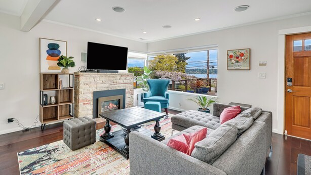 A modern living room with a fireplace, comfortable seating, and a large window offering a view of the outdoors. - 4bd w/ Lake Views and Chef's Kitchen (Seattle)