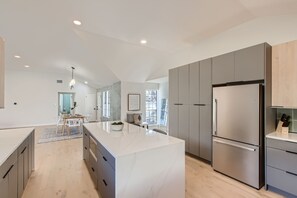 A modern kitchen with a large island, grey cabinets, and a stainless steel refrigerator. - Modern 4bd w/ Pool, Outside dining, Gourmet kitchen (Austin)