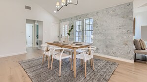 Moderni ruokailutila, jossa on puinen pöytä ja valkoiset tuolit, kuviollinen matto ja suuri ikkuna, josta on kaunis näköala.