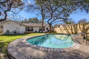 A backyard with a swimming pool, a wooden fence, and a house.