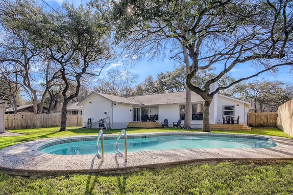 A backyard with a swimming pool, a house, and surrounding trees.
