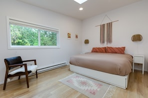 Un dormitorio con cama, una silla, un ventanal y un adorno en la pared.