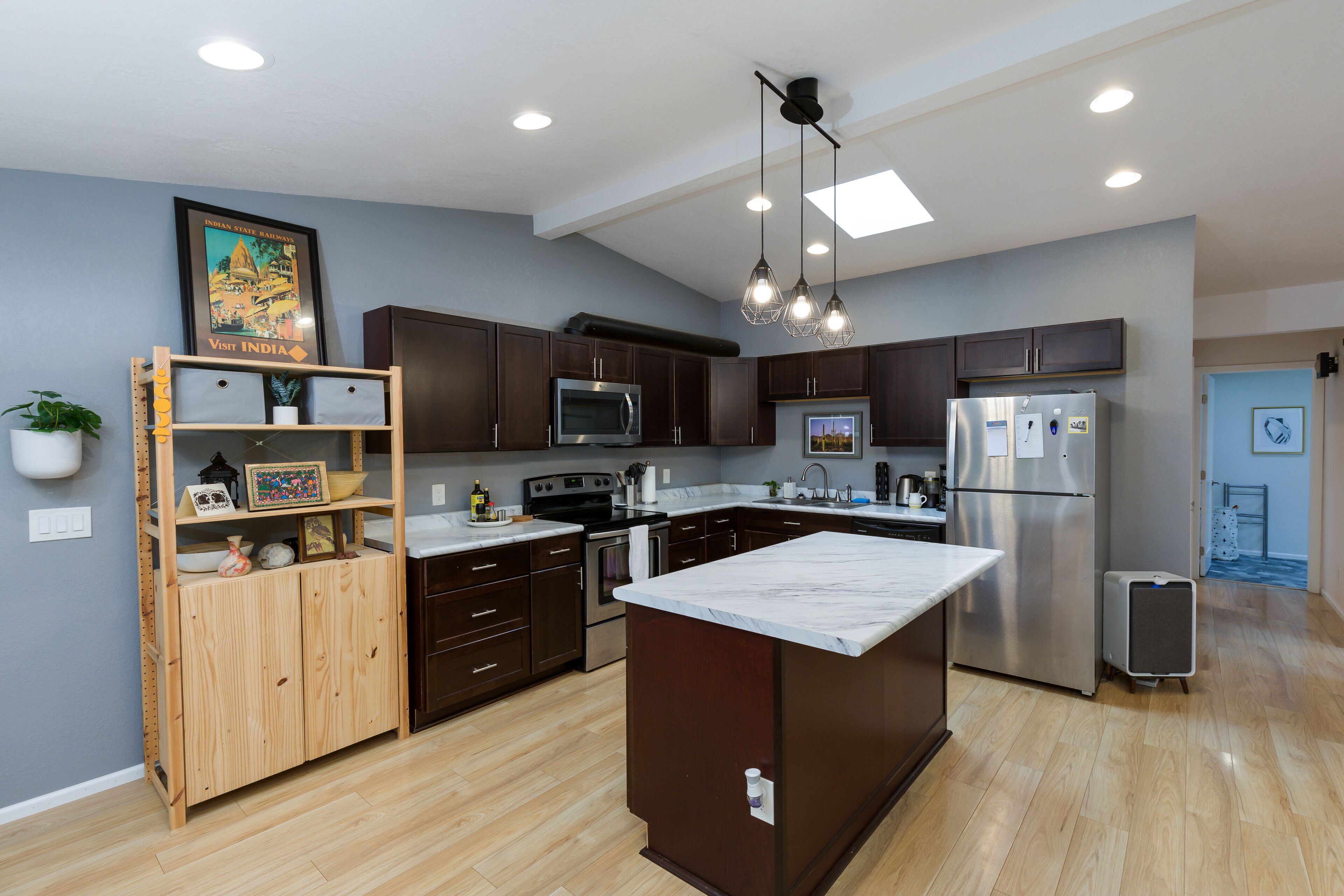 A modern kitchen with dark wood cabinets, stainless steel appliances, and a marble island.