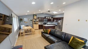 Una cocina moderna con armarios oscuros, una isla central y un comedor con mesa y banco de madera.