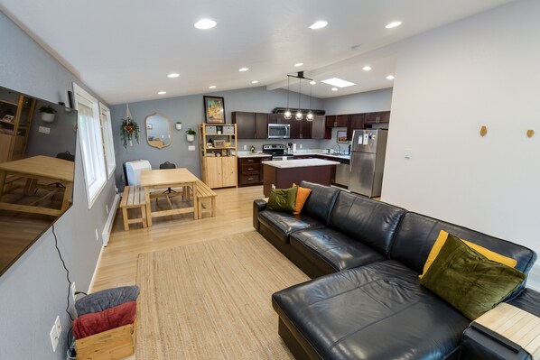 Una cocina moderna con armarios oscuros, una isla central y un comedor con mesa y banco de madera.
