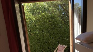Una habitación pequeña y de distribución abierta con una cama, una silla y vistas a un seto verde.
