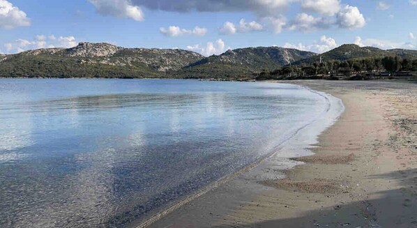 A beach with clear water, a sandy shore, and mountains in the background.