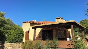 Un edificio de una planta con techo de tejas rojas, paredes de piedra y un porche de madera.