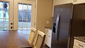 Una cocina con mesa de madera, sillas, un refrigerador y una ventana con vistas al exterior.