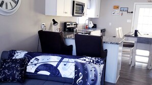 Una sala de estar moderna con un sofá, una mesa de centro y una cocina con armarios blancos y un microondas.