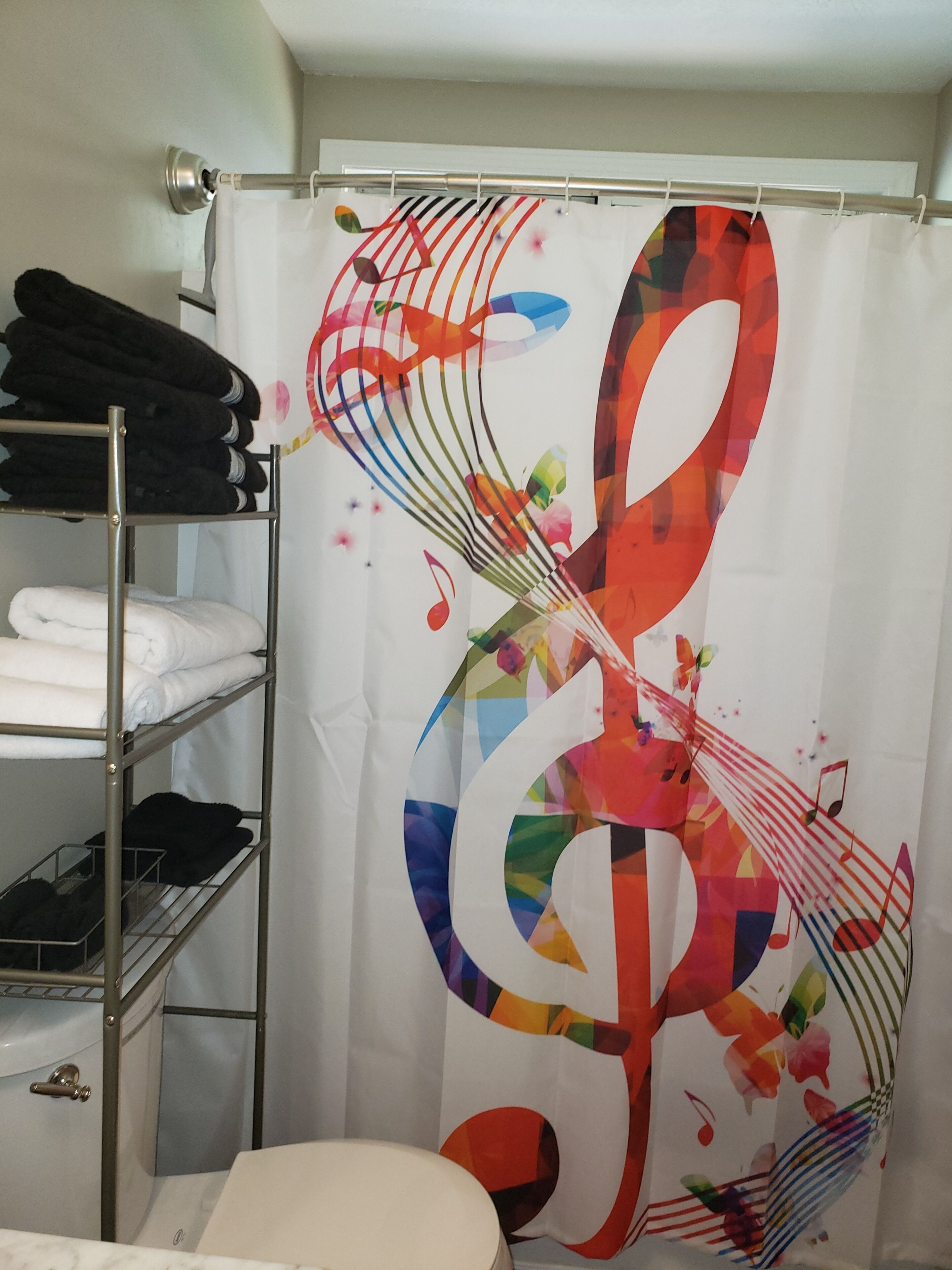 Een badkamer met een douchegordijn met een kleurrijk ontwerp van muzieknoten, een metalen handdoekrek met opgevouwen handdoeken, en een witte wastafel.