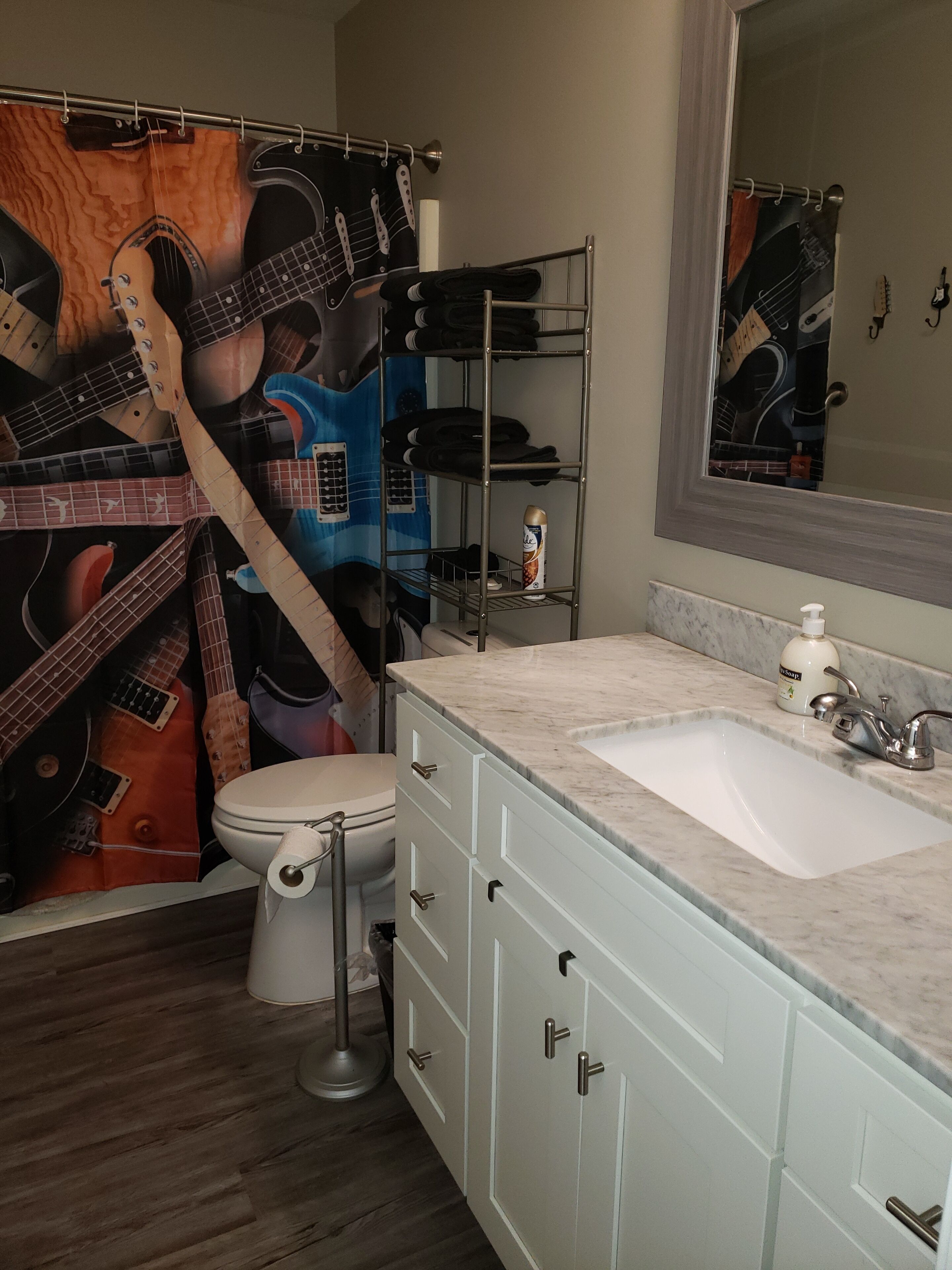A bathroom with a guitar-themed shower curtain, a toilet, a sink with a soap dispenser, and a mirror above the sink.