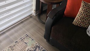Een gezellige woonkamer met een donkerbruine bank, een rode kussens, een klein rond tafeltje met een lamp en een speelgoedtruck, en een plant in een pot.