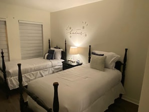 Una camera d'albergo con due letti singoli, un comodino con una lampada e una decorazione a parete con la scritta 'kindness'.