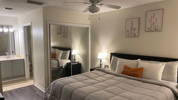 Een slaapkamer met een bed, nachtkastje, spiegel, inloopkast en een badkamer met wastafel.