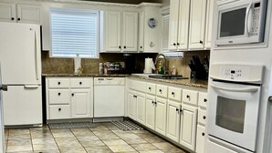 Een keuken met witte kastjes, een roestvrijstalen prullenbak en een magnetron.