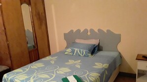 A bed with a floral bedspread, a pillow, and a green and white blanket. - Royal Savanna Inn Hotel (Savanna la Mar)