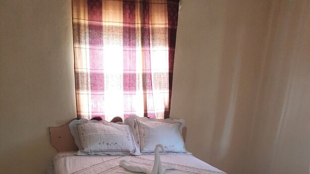 A neatly made bed with a swan-shaped pillow and a geometric-patterned bedspread. - Royal Savanna Inn Hotel (Savanna la Mar)