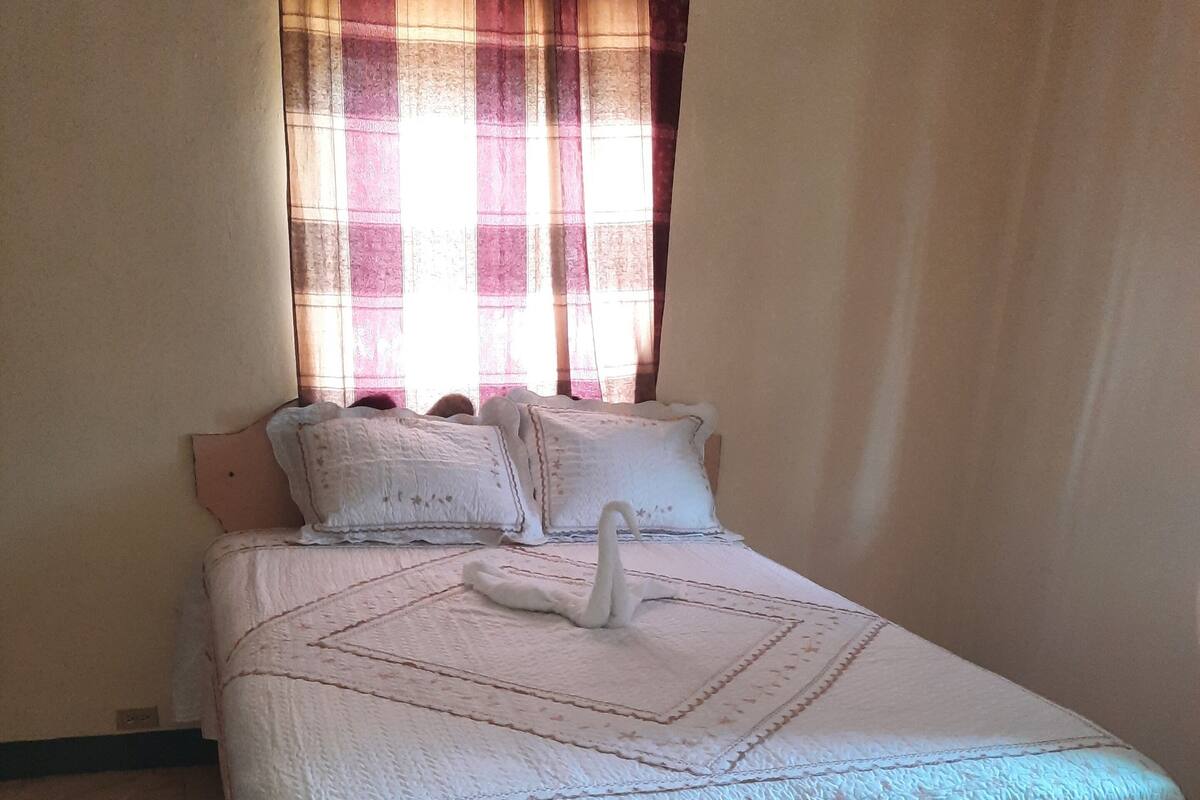 Una cama bien hecha con un almohadón con forma de cisne y una colcha de estampado geométrico.
