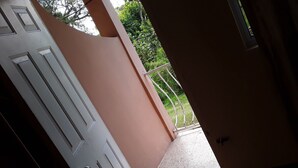 An interior corridor with a white door, a pink wall, and a view of greenery outside. - Royal Savanna Inn Hotel (Savanna la Mar)