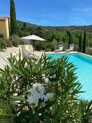 Una piscina con lettini e un ombrellone, circondata da vegetazione e colline sullo sfondo.