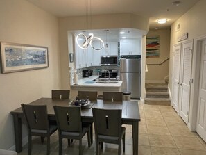 Kitchen features a central island with sink and refrigerator, adjacent dining area with table and chairs, and a staircase to the upper level.