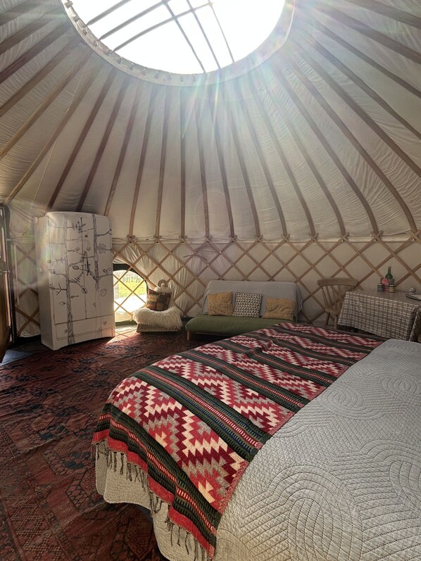 A yurt interior with a bed, a small table, and a cabinet. - Dragon Orchard Retreat (Ledbury)