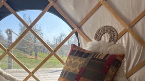A bed with a fluffy white cover, a patchwork pillow, and a woven basket at the foot. - Dragon Orchard Retreat (Ledbury)